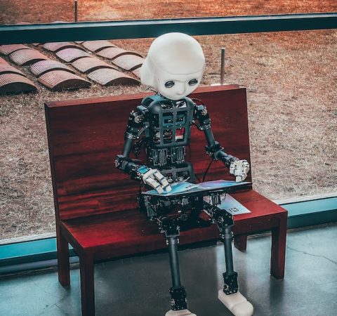 little robot using a tablet on a wooden bench outside